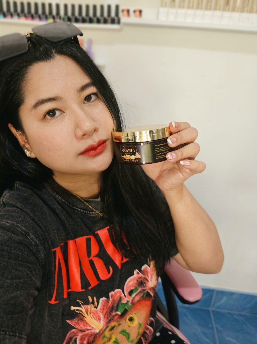 Thai customer holding Arokaya herbal scrub amber jar at a nail salon in Thailand